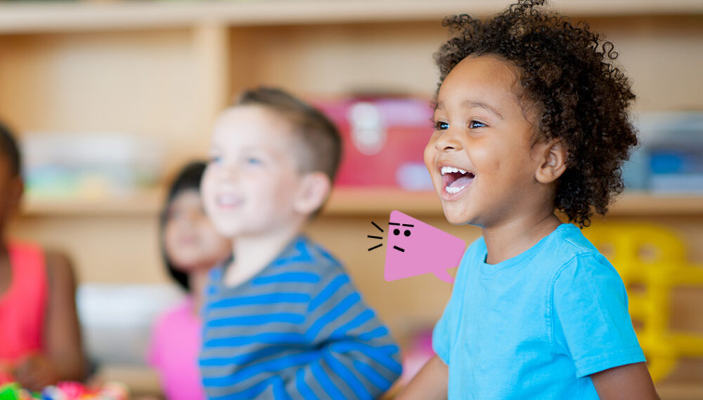 Young boy sat in classroom smiling with a graphic overlay of a pink character with a stern look. The character has three black lines by it's mouth to indicate it's shouting.